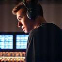 Portrait of a male audio engineer with headphones on, confidently working at a sound mixing board.
